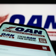 A phone with OAN One America News App held close to the camera across from a blurred TV screen with OAN on it